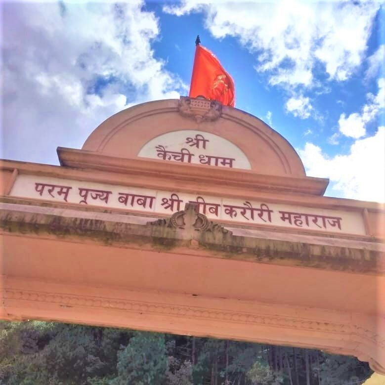 "Param Pujya Baba Shri Neeb Karori Maharaj" written on brownish red coloured Shri Kainchi Dham gate with Saffron Flag at