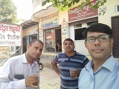Mukesh Dwivedi wearing glasses taking selfie while TN in a cream shirt & a mobile in his breast pocket and Chandrabhall in midum thick three blue colour shades circled linings giving pose for the photo with a cup of black tea in their respective hands.